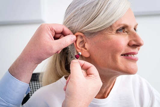 Eine Frau bekommt ein modernes Hörgerät angepasst und lächelt zufrieden.